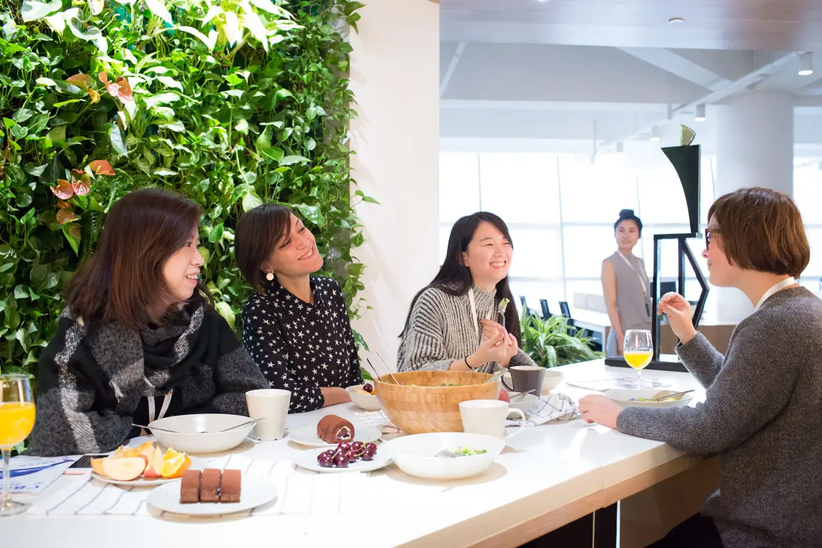 Members talking over lunch beside a green plant wall