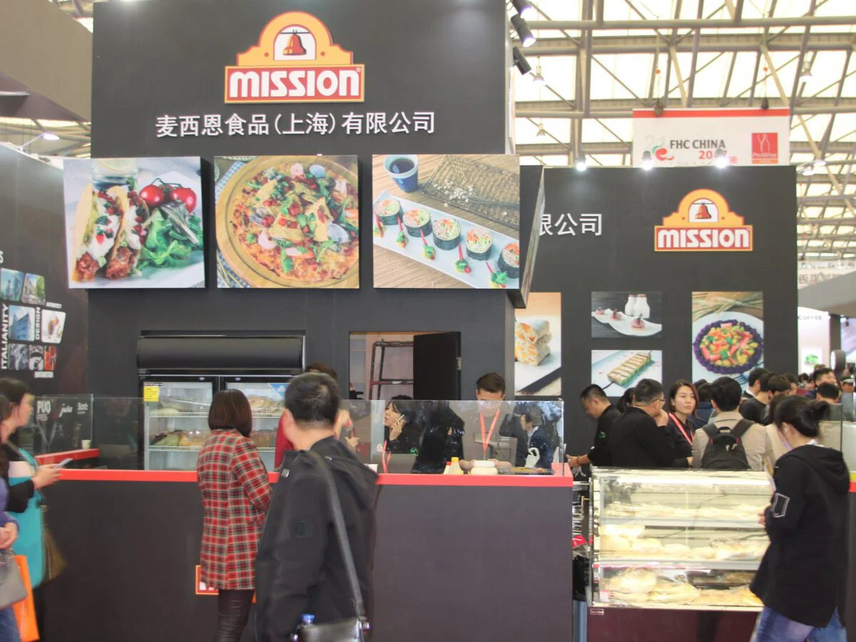 Mission Foods stand at HOTELEX Shanghai: black towers with the Mission bell logo, backlit food photography and a busy red tasting counter