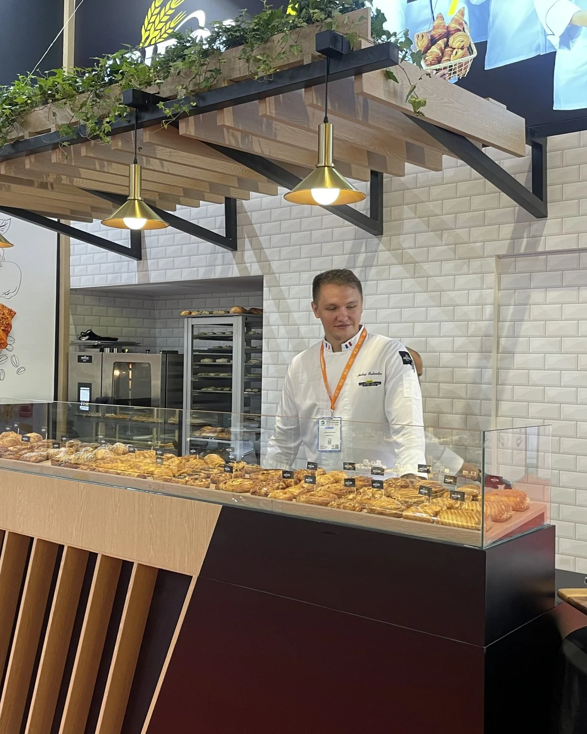 Bridor chef behind a glass counter of fresh viennoiserie, under brass pendant lights and a timber pergola