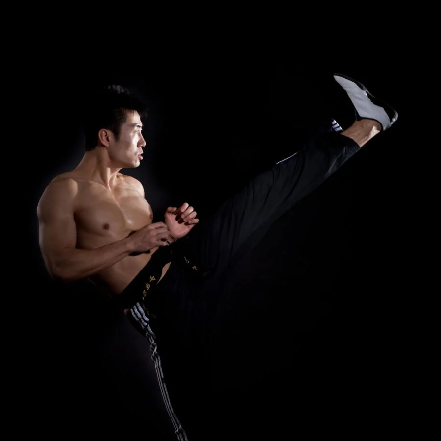 Martial artist in black training trousers throwing a high kick